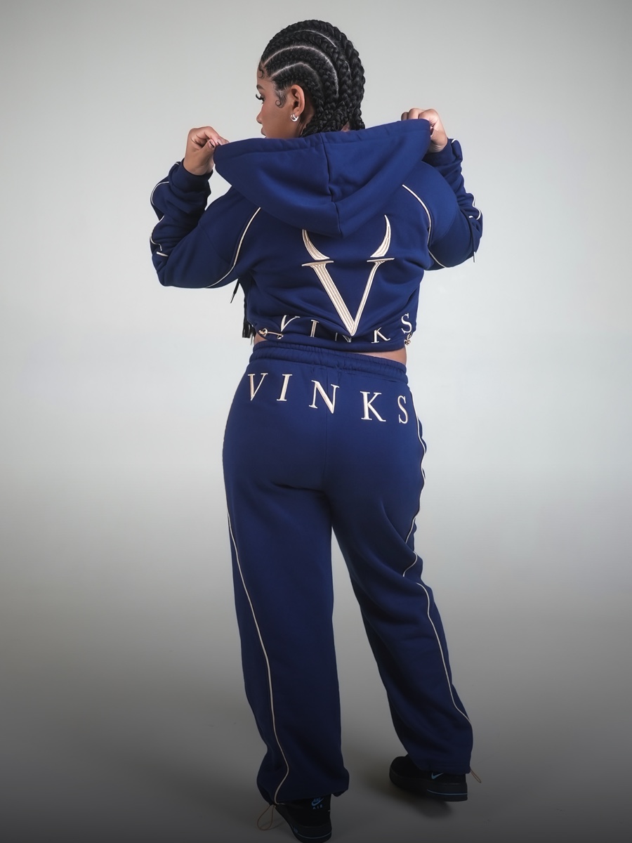 Modella di spalle in completo VINKS blu navy, con ricami V e VINKS color oro su felpa e pantalone