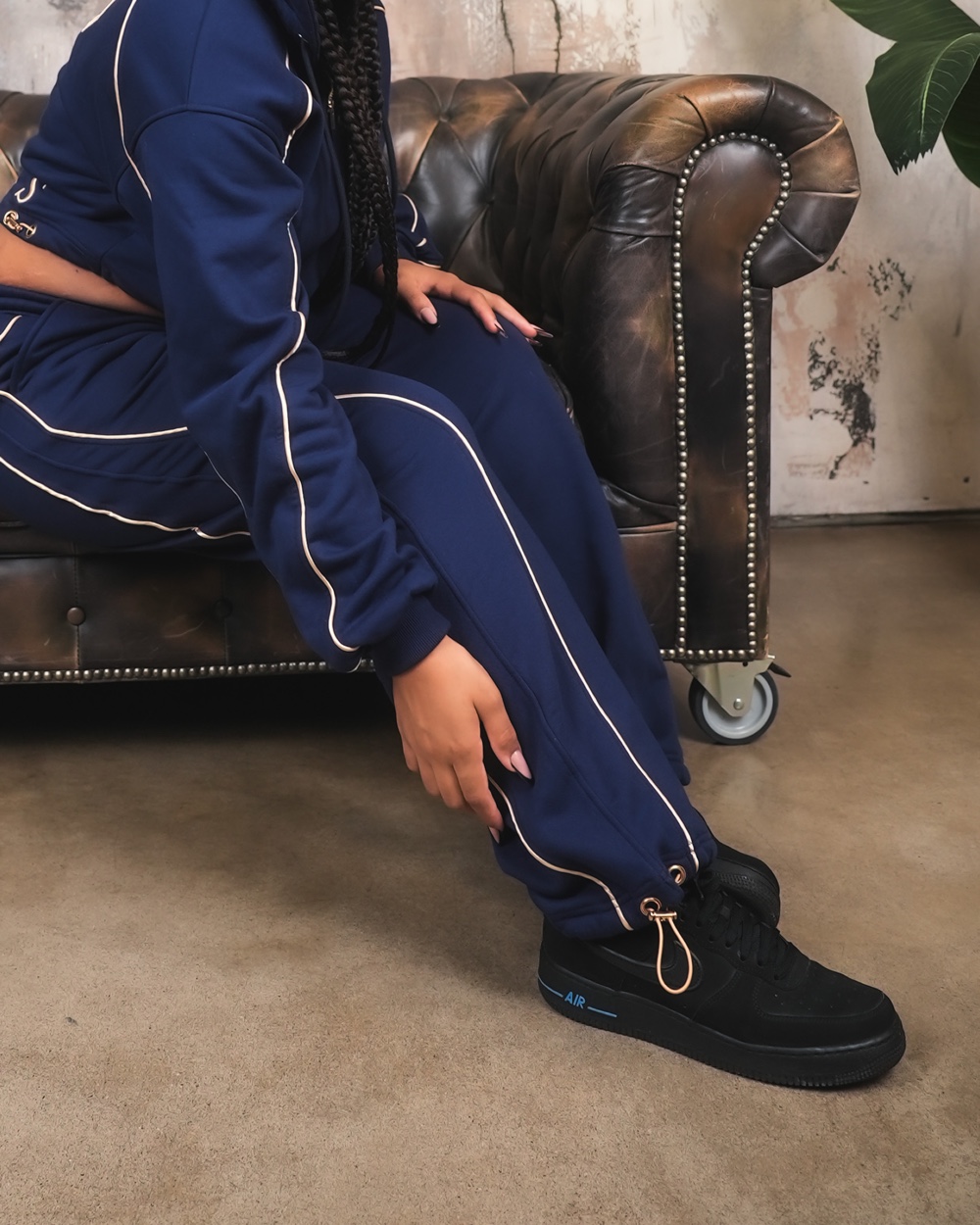 Pantalone VINKS blu navy con profili oro e coulisse dorata alla caviglia, su un chesterfield in pelle