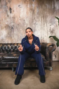 Modella seduta su un divano chesterfield in pelle con il completo VINKS blu navy e dettagli oro
