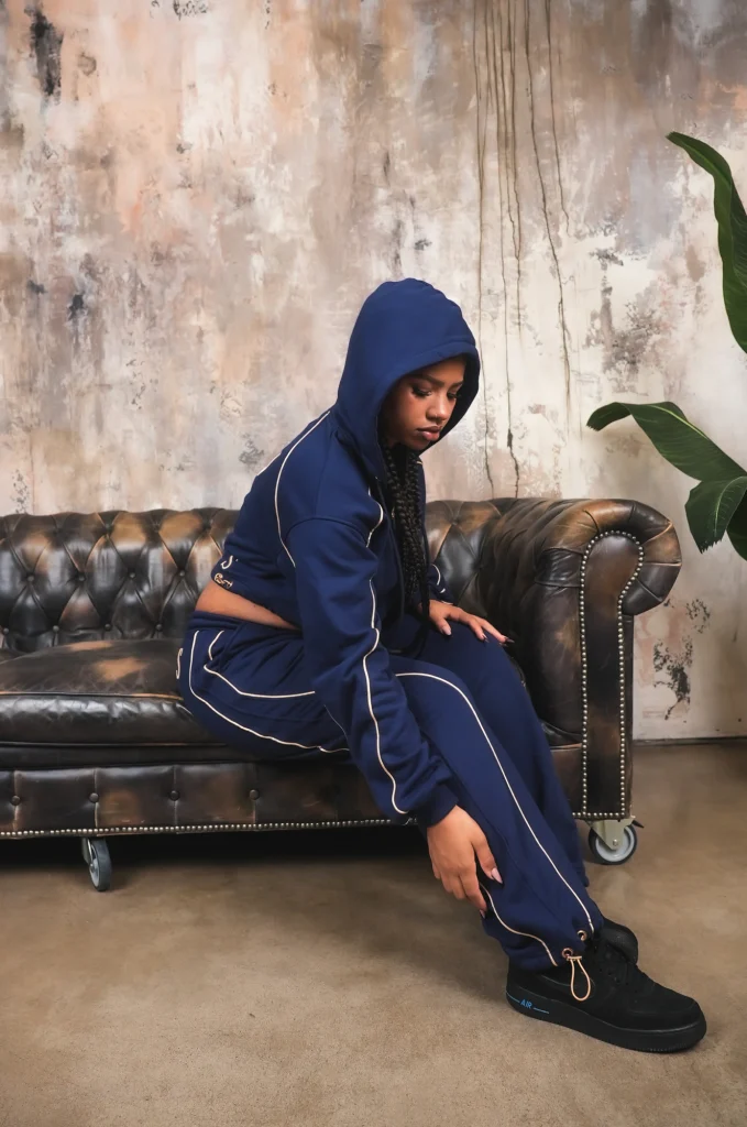 Modella con cappuccio alzato seduta di profilo su un chesterfield, completo VINKS blu navy con profili oro