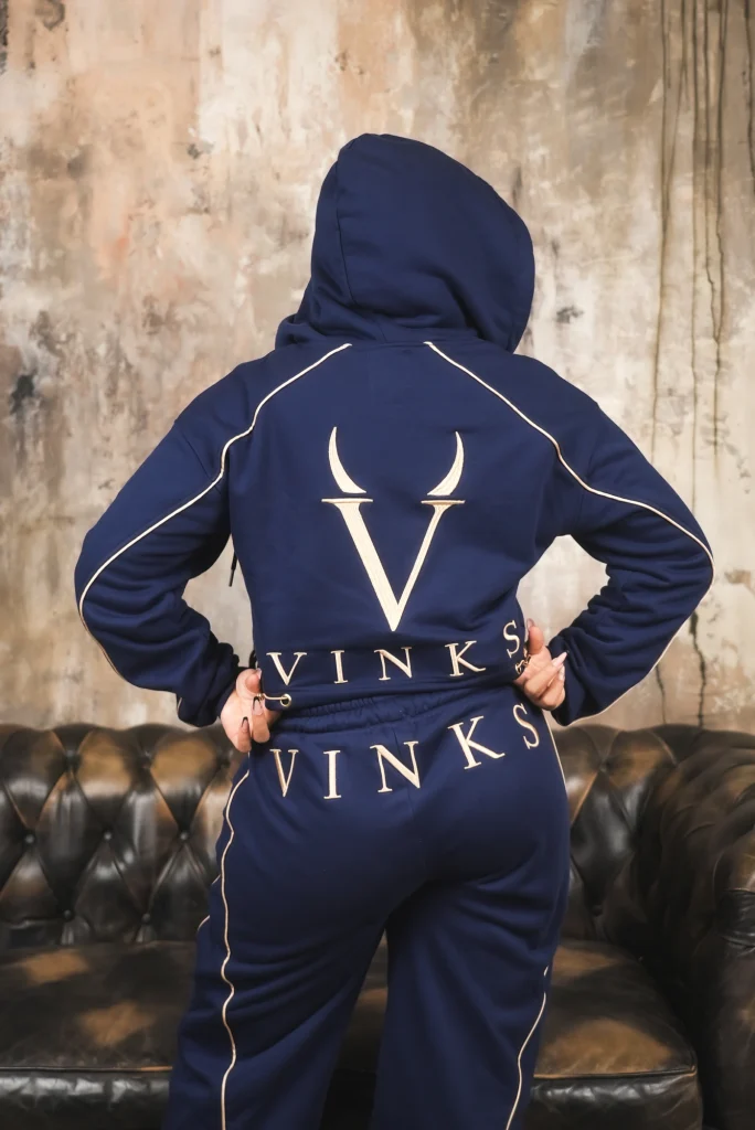 Modella di spalle davanti a un chesterfield, con monogramma V e scritta VINKS ricamati oro sul completo blu navy