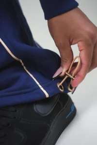 Mano che regola la coulisse con stopper dorato alla caviglia del pantalone VINKS blu navy con profilo oro
